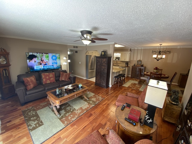 living area with crown molding, a textured ceiling, ceiling fan with notable chandelier, and wood finished floors