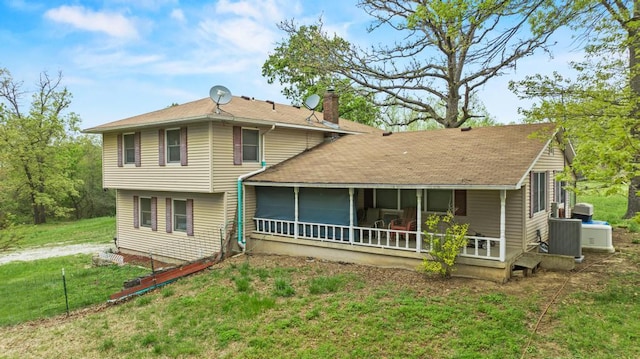 rear view of house featuring a lawn, a chimney, a shingled roof, and a sunroom