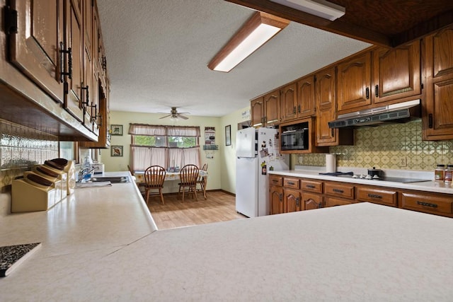 kitchen with light countertops, tasteful backsplash, freestanding refrigerator, and under cabinet range hood