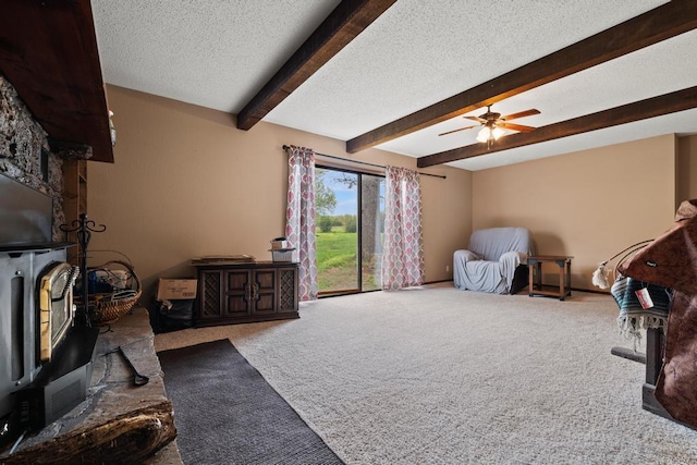 living room with a wood stove, beam ceiling, ceiling fan, a textured ceiling, and carpet flooring