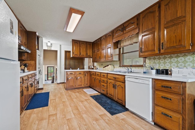 kitchen with tasteful backsplash, a sink, light countertops, light wood-style floors, and white appliances