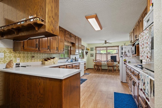 kitchen featuring a peninsula, white appliances, light wood-type flooring, light countertops, and a ceiling fan