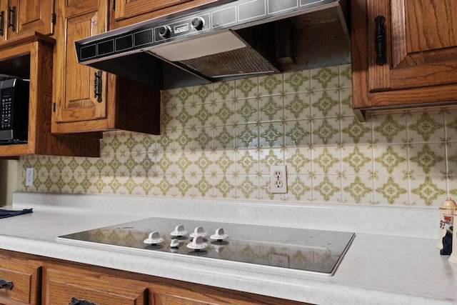 kitchen featuring under cabinet range hood, brown cabinets, black appliances, and light countertops