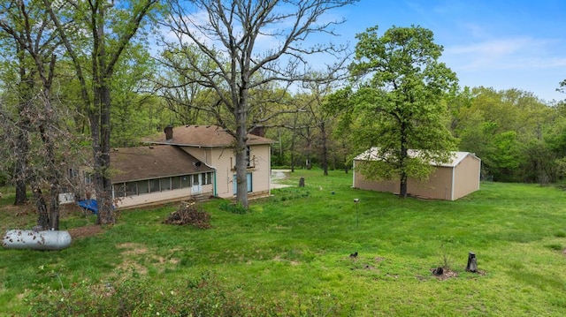 view of yard featuring a storage shed, an outdoor structure, a sunroom, and a forest view