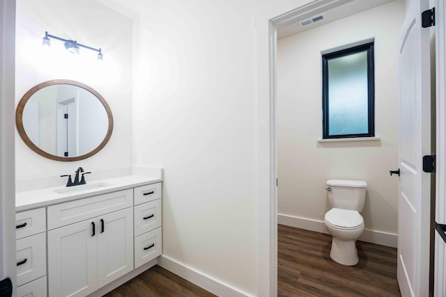 bathroom with vanity, toilet, baseboards, wood finished floors, and visible vents
