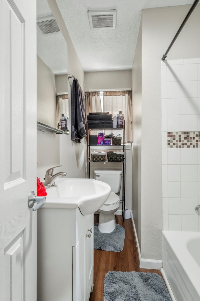bathroom featuring vanity, visible vents, wood finished floors, toilet, and a textured ceiling