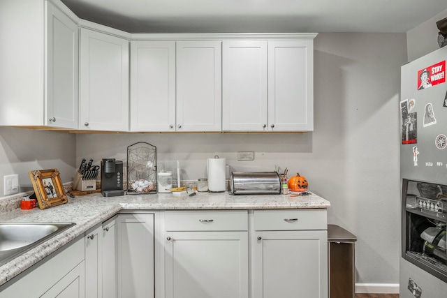 kitchen featuring stainless steel refrigerator with ice dispenser, a sink, and white cabinetry