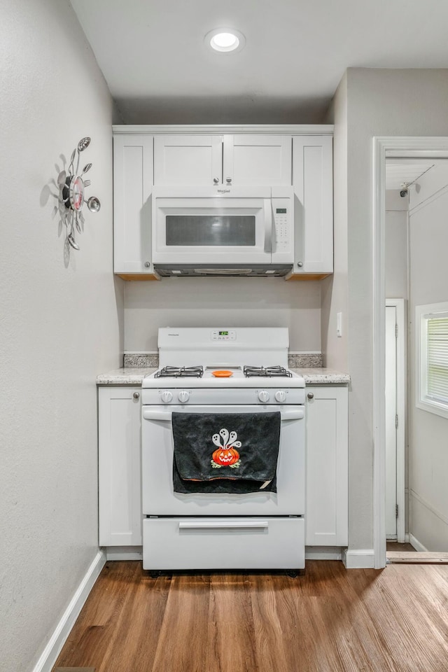kitchen featuring baseboards, wood finished floors, white cabinets, and white appliances
