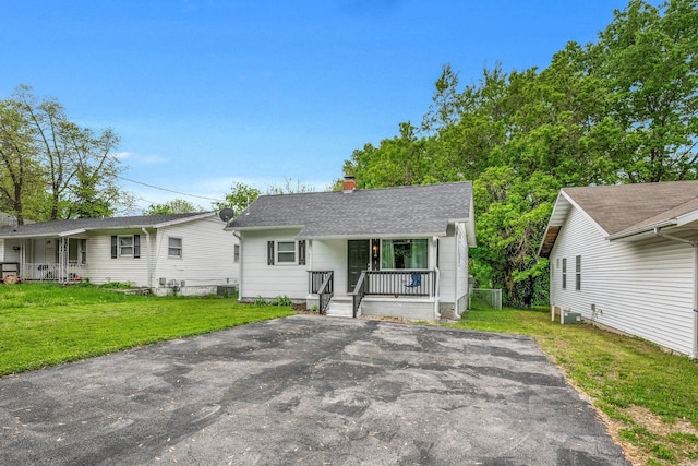 bungalow-style house with roof with shingles, a front lawn, a porch, a chimney, and driveway