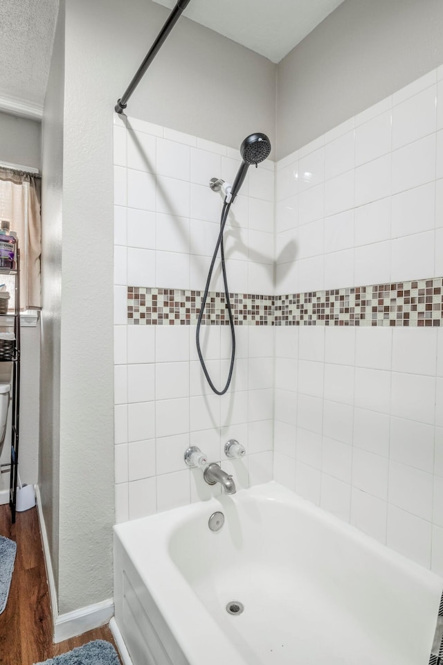 bathroom featuring tub / shower combination, baseboards, and wood finished floors