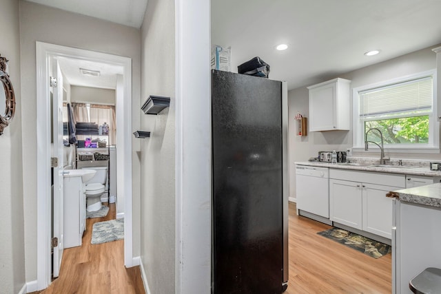 kitchen featuring dishwasher, a sink, freestanding refrigerator, light wood finished floors, and white cabinetry