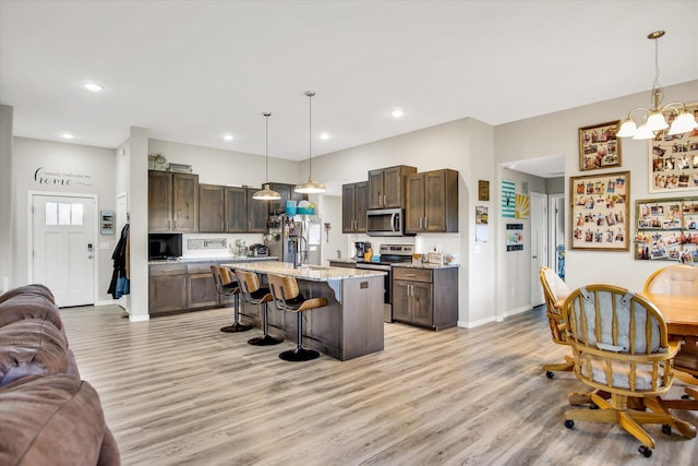 kitchen featuring dark brown cabinets, a breakfast bar, open floor plan, light wood finished floors, and appliances with stainless steel finishes