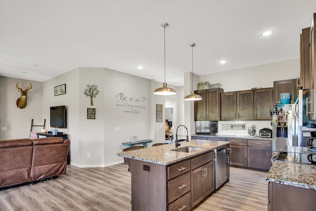 kitchen featuring light stone countertops, a sink, open floor plan, light wood-style floors, and stainless steel appliances