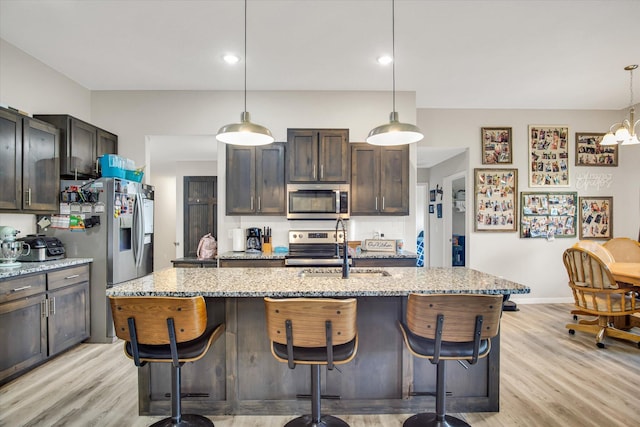 kitchen with a sink, light wood-style flooring, appliances with stainless steel finishes, and a breakfast bar area