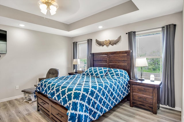 bedroom featuring baseboards, multiple windows, a tray ceiling, and light wood-style floors