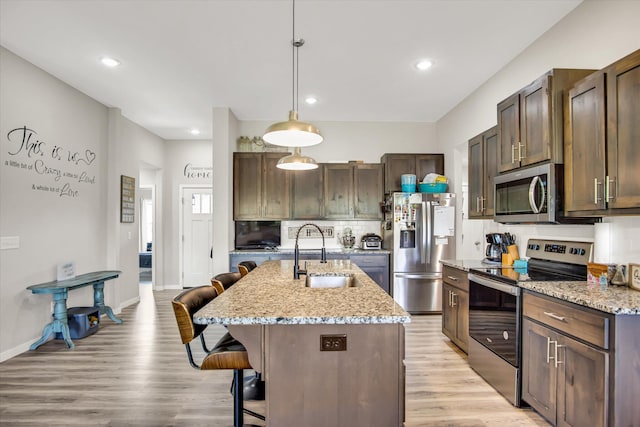 kitchen with hanging light fixtures, appliances with stainless steel finishes, a sink, light wood-style floors, and a breakfast bar area