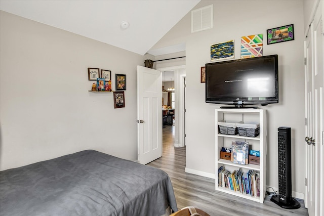 bedroom featuring visible vents, baseboards, lofted ceiling, and wood finished floors