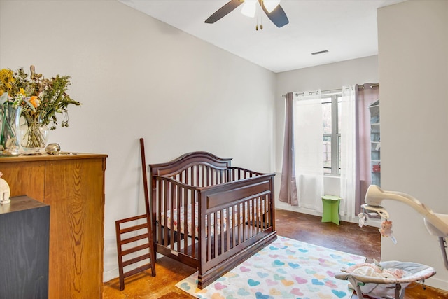 bedroom featuring visible vents, concrete flooring, baseboards, ceiling fan, and a crib