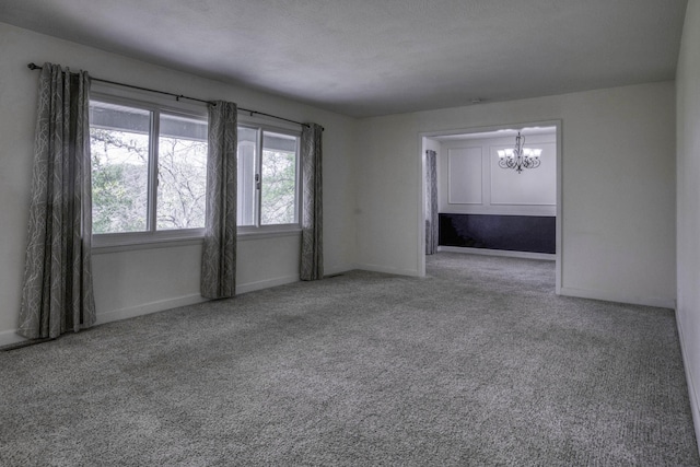 spare room with carpet flooring, baseboards, and an inviting chandelier