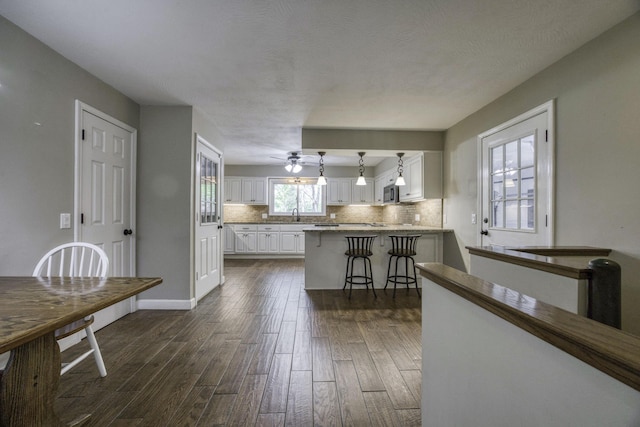 kitchen with ceiling fan, a breakfast bar, white cabinetry, dark wood-type flooring, and backsplash