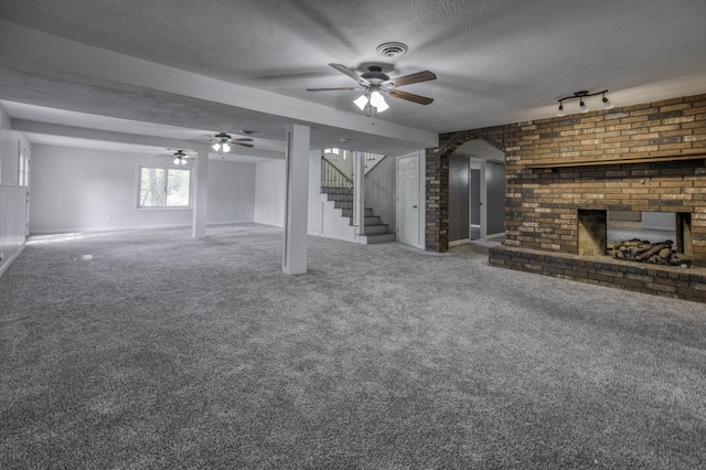 interior space featuring carpet floors, stairs, a brick fireplace, a textured ceiling, and a ceiling fan