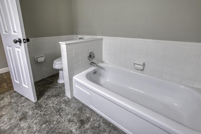 full bath featuring toilet, wainscoting, and a garden tub
