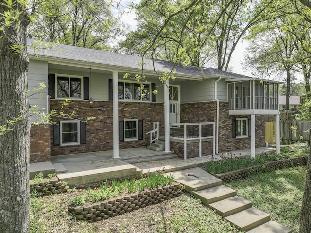 rear view of house with brick siding, fence, a sunroom, and a patio