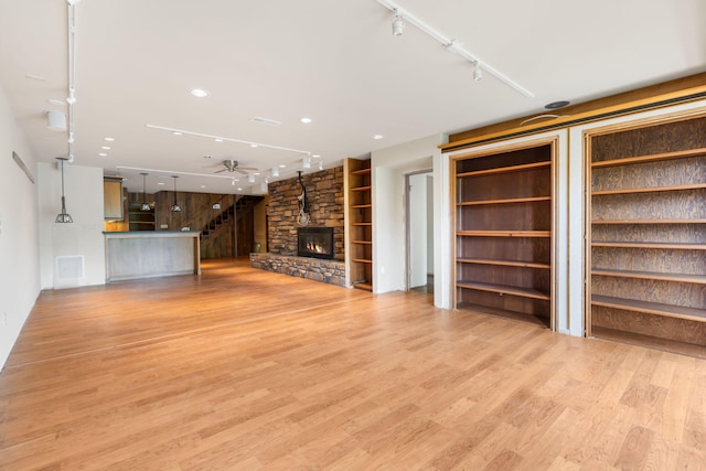 unfurnished living room featuring ceiling fan, a fireplace, light wood-type flooring, track lighting, and stairs