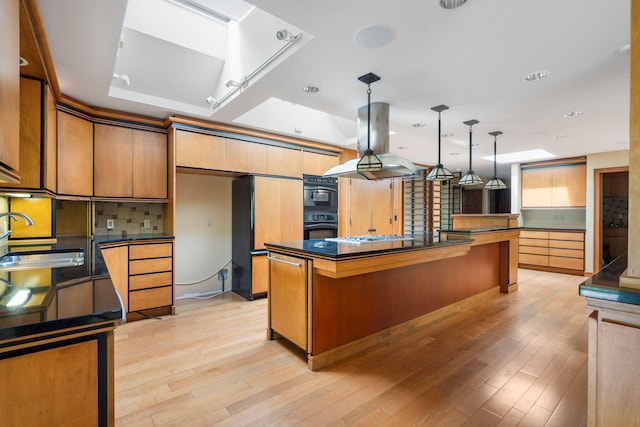 kitchen with island exhaust hood, dark countertops, a center island, light wood-type flooring, and a sink