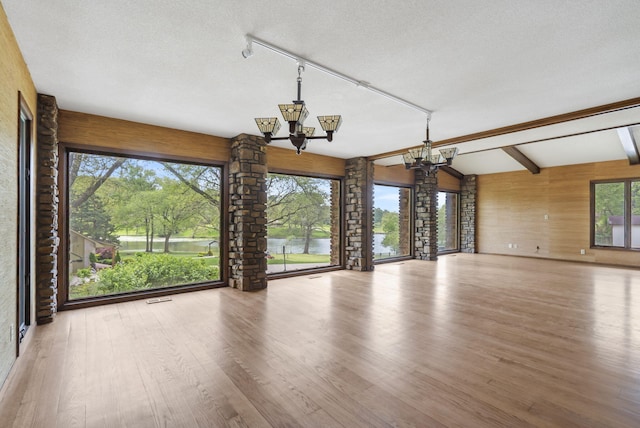 unfurnished room with a textured ceiling, wood finished floors, lofted ceiling with beams, a chandelier, and a water view