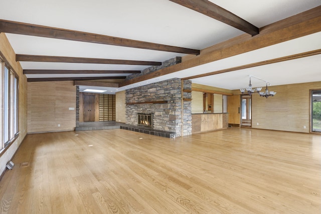 unfurnished living room featuring beam ceiling, a notable chandelier, a stone fireplace, and wood finished floors