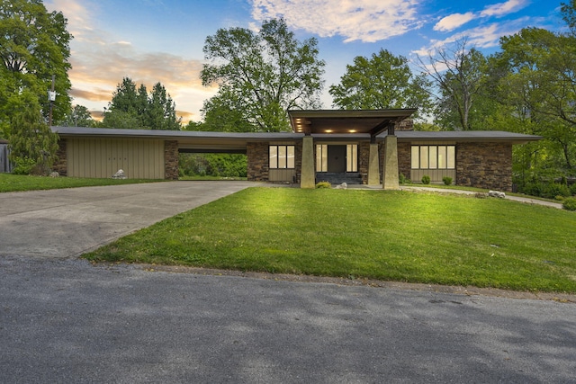 prairie-style house with an attached carport, driveway, a front lawn, and stone siding