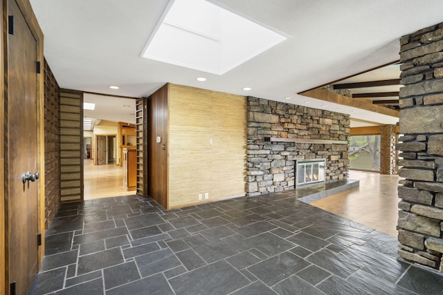 unfurnished living room with recessed lighting, a skylight, stone finish flooring, and a stone fireplace