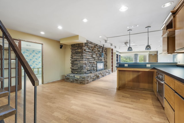 kitchen featuring dark countertops, light wood-style floors, a fireplace, stainless steel oven, and a peninsula