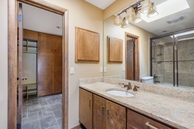 bathroom featuring visible vents, stone finish flooring, a shower with shower door, and vanity