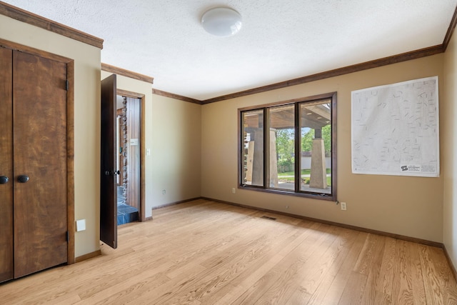 unfurnished bedroom with crown molding, a textured ceiling, light wood-style flooring, and baseboards