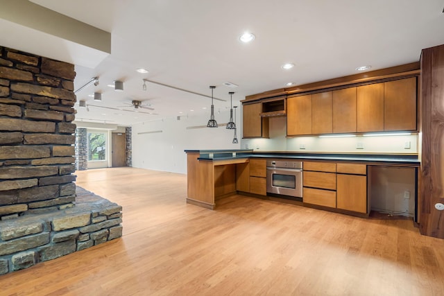 kitchen featuring open floor plan, light wood-style flooring, dark countertops, and oven