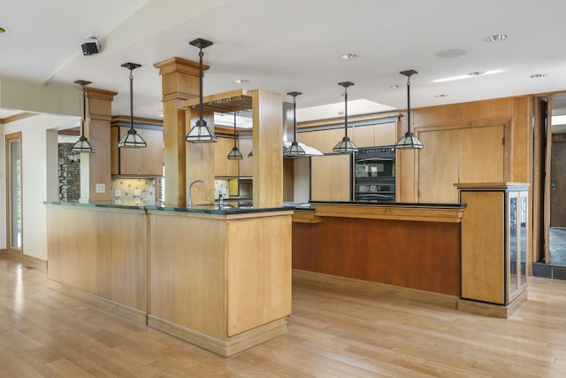 kitchen featuring pendant lighting, tasteful backsplash, dobule oven black, and light wood-type flooring