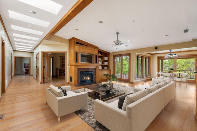 living room featuring a ceiling fan, light wood finished floors, vaulted ceiling with skylight, and a large fireplace