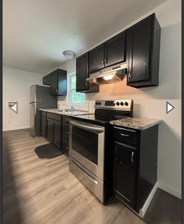 1207 W Florida St, Springfield, MO 65803 - kitchen with dark cabinetry, light wood-style flooring, under cabinet range hood, and stainless steel appliances