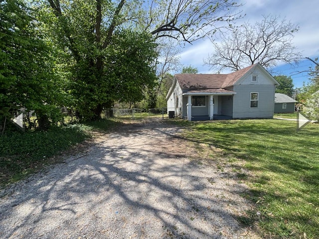 view of front of house featuring roof with shingles, fence, a front yard, and dirt driveway