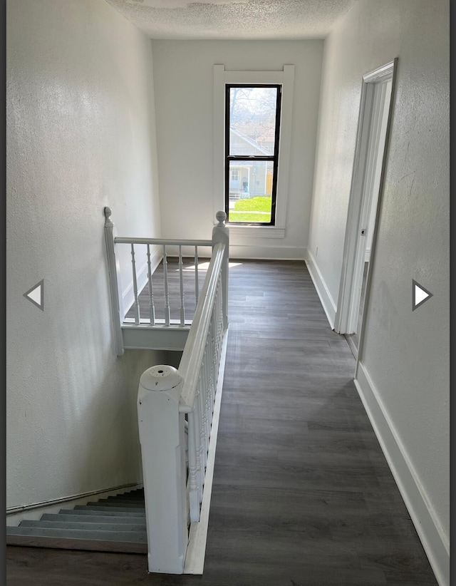 corridor featuring baseboards, a textured wall, an upstairs landing, and wood finished floors