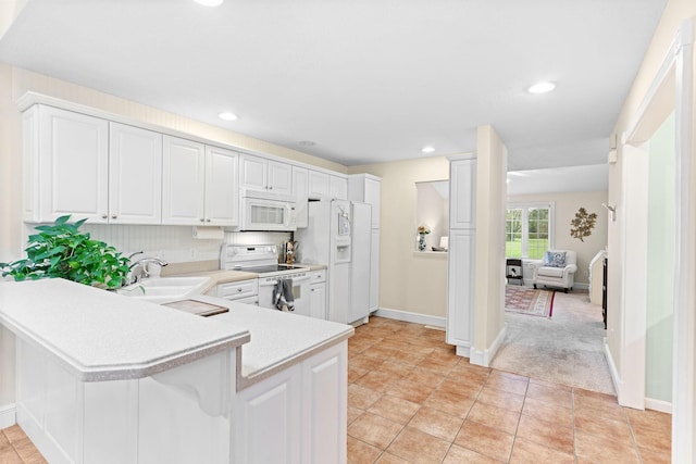 kitchen featuring a sink, white appliances, light countertops, a peninsula, and baseboards
