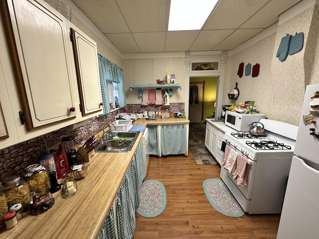 kitchen with white appliances, a drop ceiling, wallpapered walls, a sink, and light wood finished floors