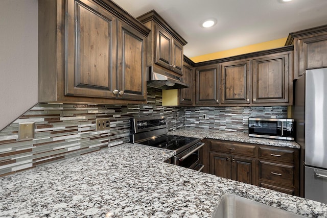 kitchen with dark brown cabinetry, light stone counters, stainless steel appliances, backsplash, and under cabinet range hood