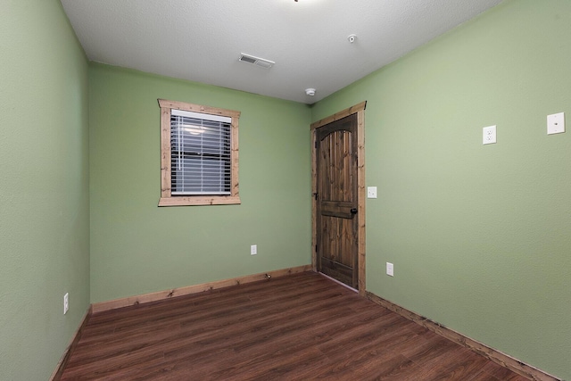 unfurnished room featuring baseboards, dark wood-style floors, and visible vents