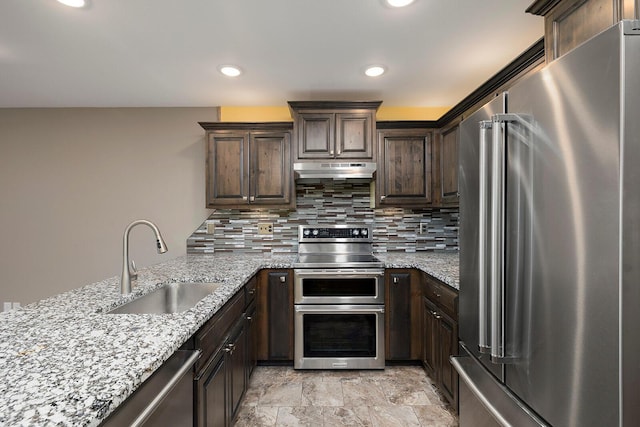 kitchen with dark brown cabinets, light stone countertops, a sink, stainless steel appliances, and under cabinet range hood