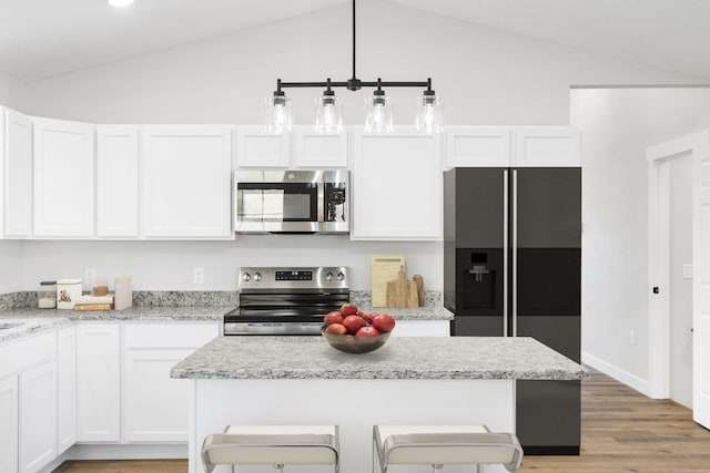 kitchen featuring appliances with stainless steel finishes, vaulted ceiling, light wood-type flooring, a breakfast bar, and white cabinetry