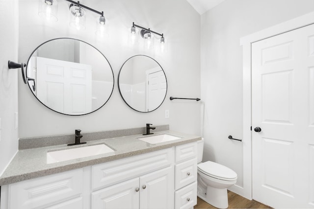 bathroom featuring double vanity, toilet, a sink, and wood finished floors