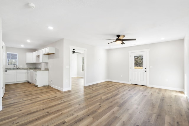 unfurnished living room with light wood-style floors, baseboards, ceiling fan, and plenty of natural light